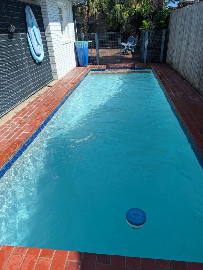 Clear blue backyard pool with red brick coping on a sunny day