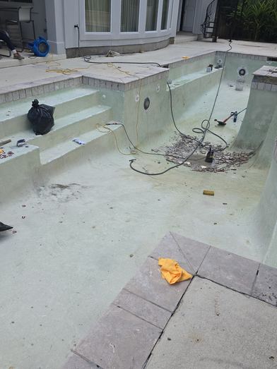 Drained pool with steps, hoses and tools laid out during prep work for resurfacing