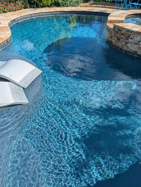 Freeform pool with stone coping, a stacked-stone spa spilling into the pool and loungers on a tanning ledge