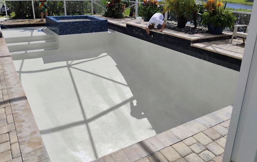 Empty pool with a fresh white plaster finish and a raised tiled spa, with a worker at the pool edge