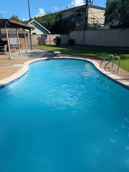 Kidney-shaped pool with a stainless steel ladder, clear blue water and a green lawn